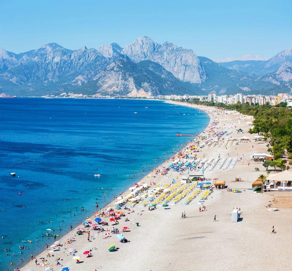 Konyaalti Beach in Antalya with sun loungers, umbrellas, and vacationers by the sea.
