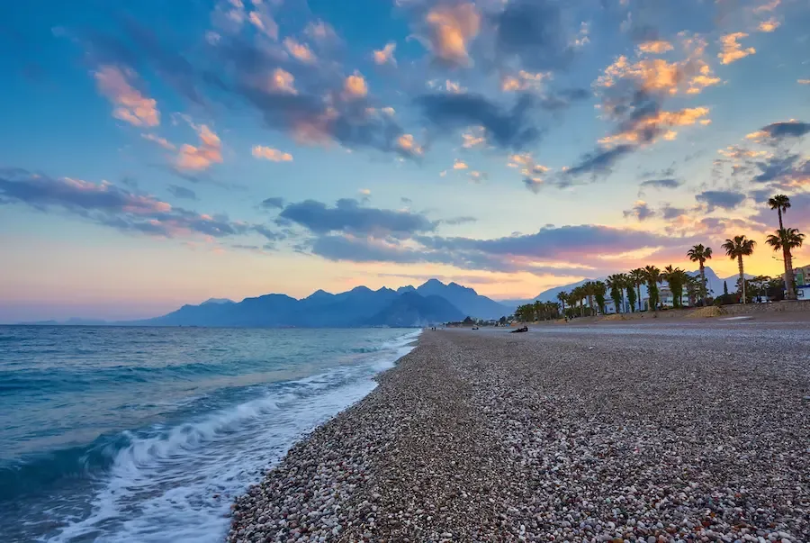 Konyaalti Beach at sunset with views of sea waves and mountain silhouettes.