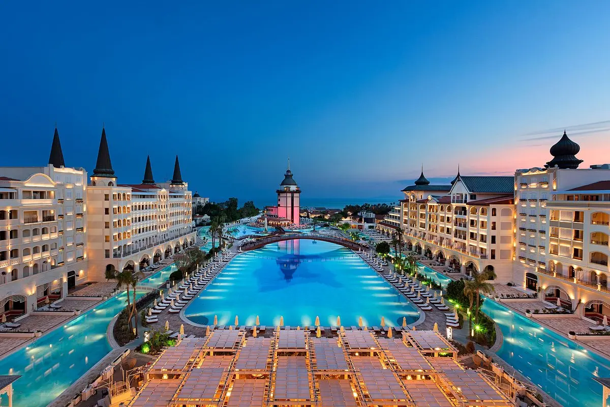 Luxurious resort hotel illuminated at dusk with a large swimming pool in Antalya.