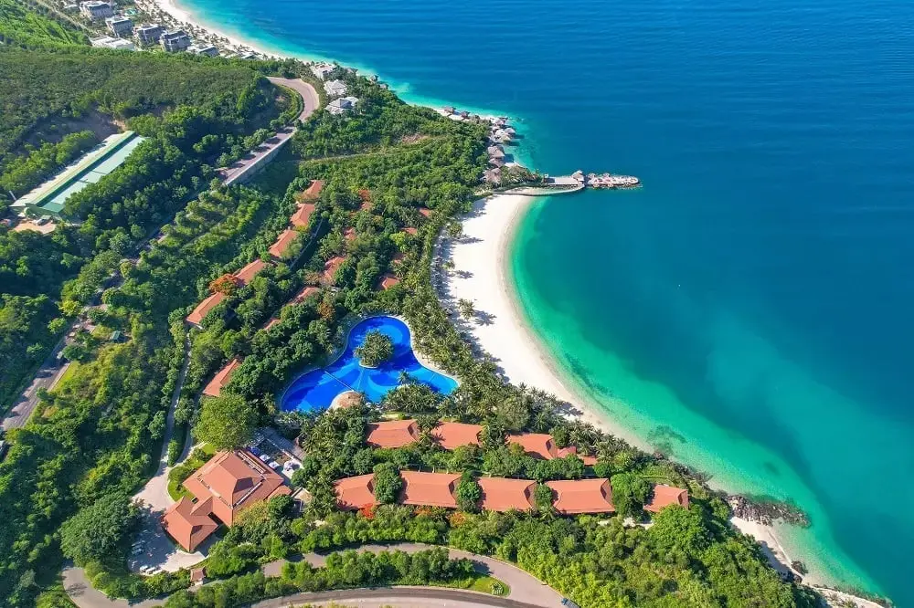Aerial view of a beachfront resort with a large blue swimming pool and tropical greenery.