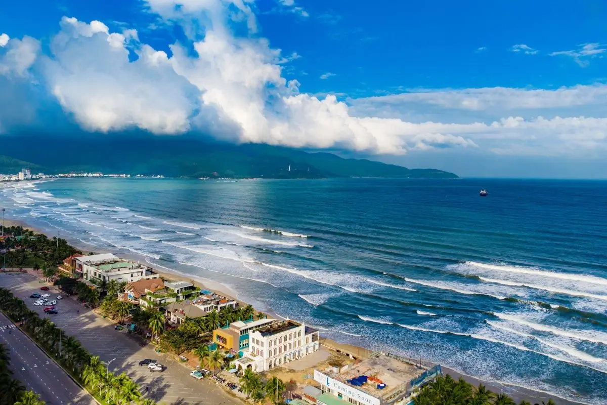 Ocean waves along the Da Nang coastline against green mountains and cloudy sky.