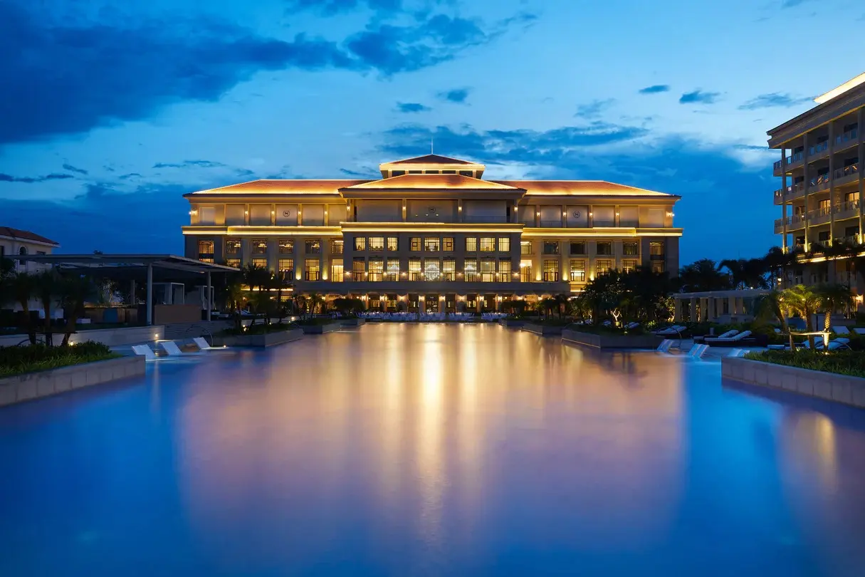 Подсвеченный главный корпус отеля Sheraton Grand Danang и бассейн в вечернее время.