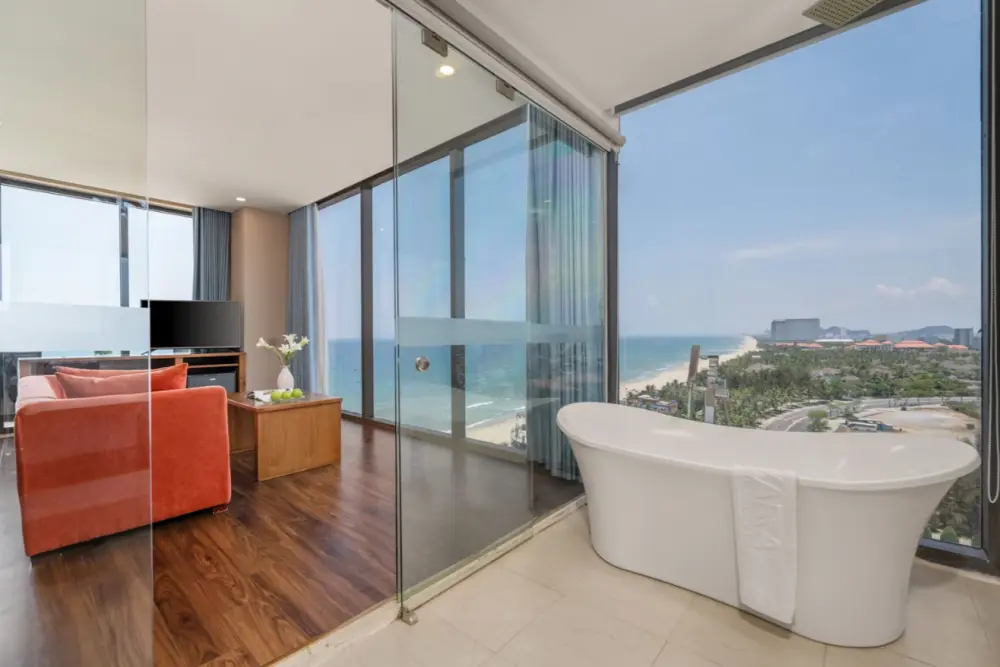 Hotel suite featuring a standalone bathtub by a floor-to-ceiling window with ocean views.
