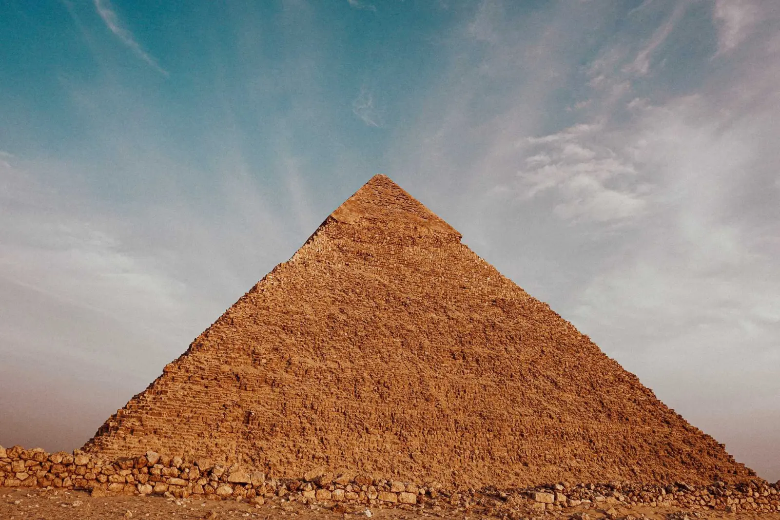 A pyramid in Giza standing under a blue sky with light clouds.