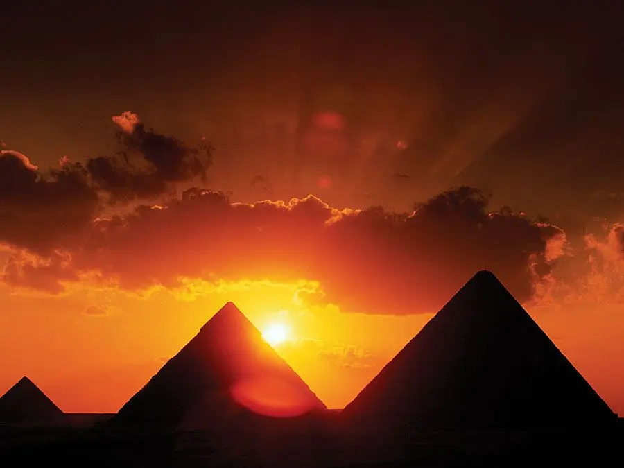 Silhouettes of the Pyramids of Giza against a vibrant orange sunset sky.