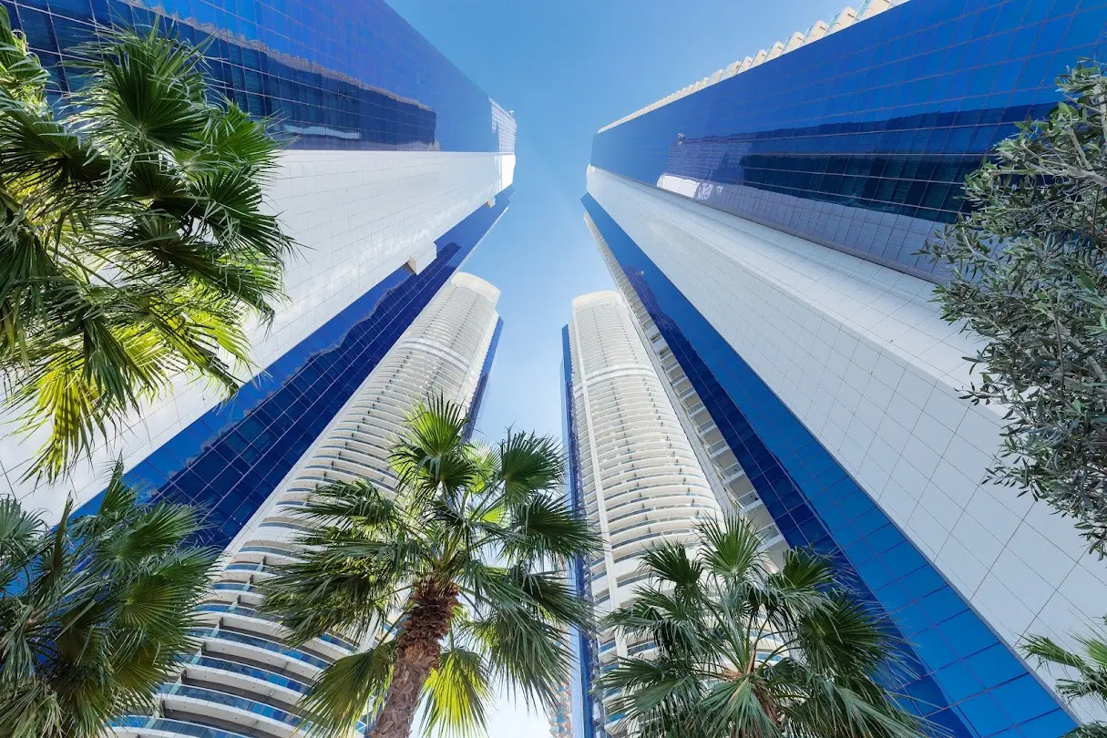 Low-angle view looking up at the glass skyscrapers of the hotel and palm trees.