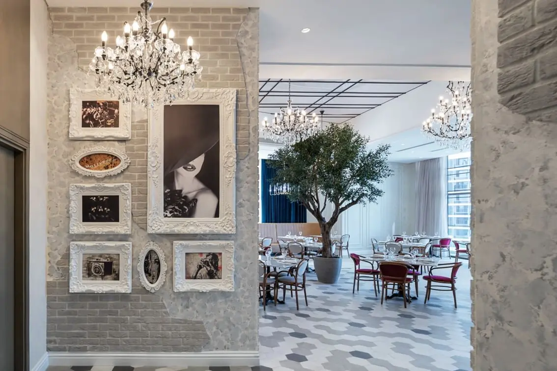 Restaurant interior with crystal chandeliers, dining tables, and wall decor.