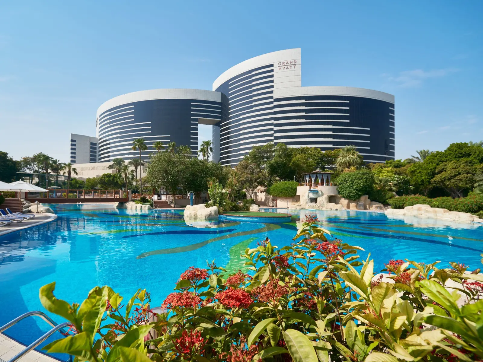 Outdoor swimming pool and main building of Grand Hyatt Dubai on a sunny day.