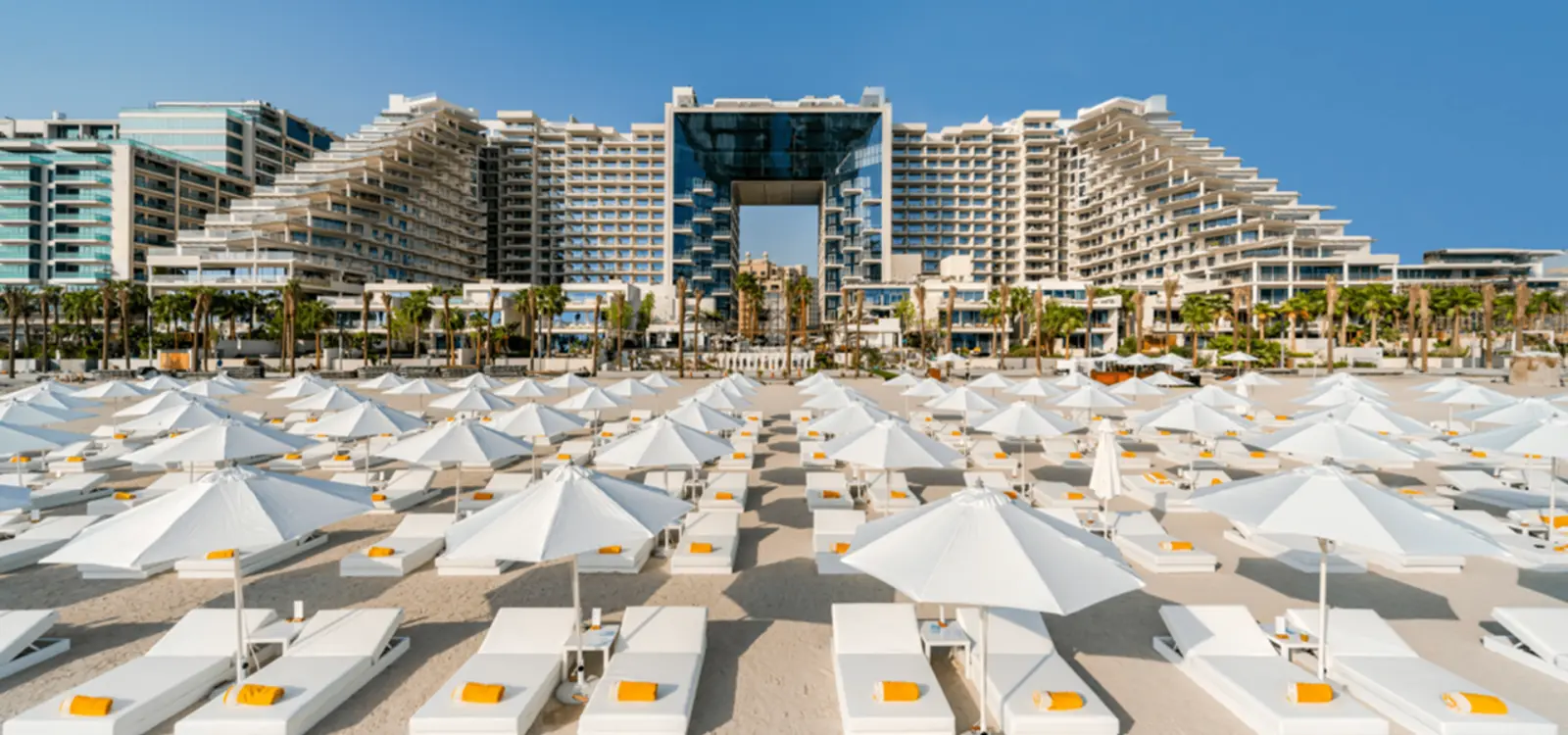 Beach with white umbrellas and sun loungers in front of the FIVE Palm Jumeirah hotel building.