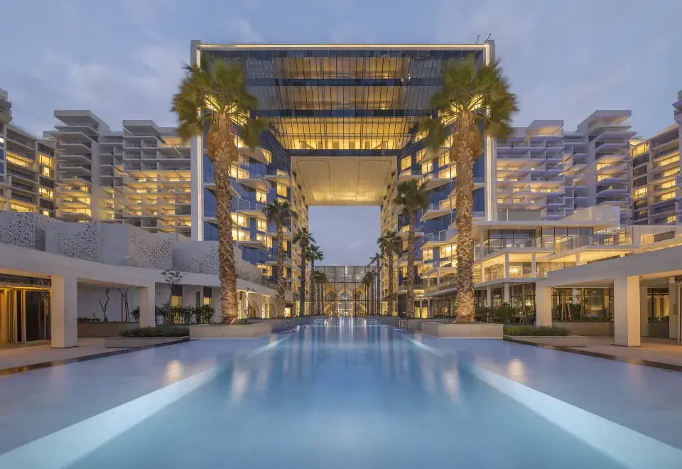 Illuminated swimming pool and reflective archway of FIVE Palm Jumeirah at dusk.