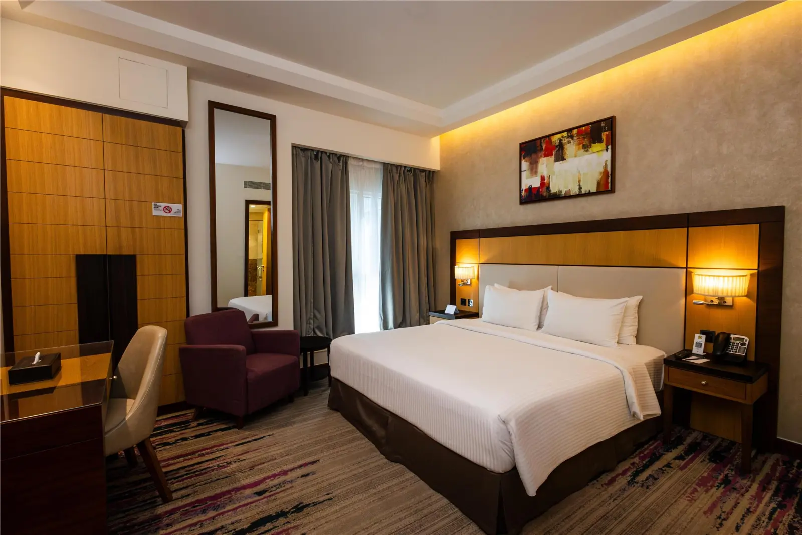 Cozy hotel room featuring a large double bed, an armchair, and warm ambient lighting.