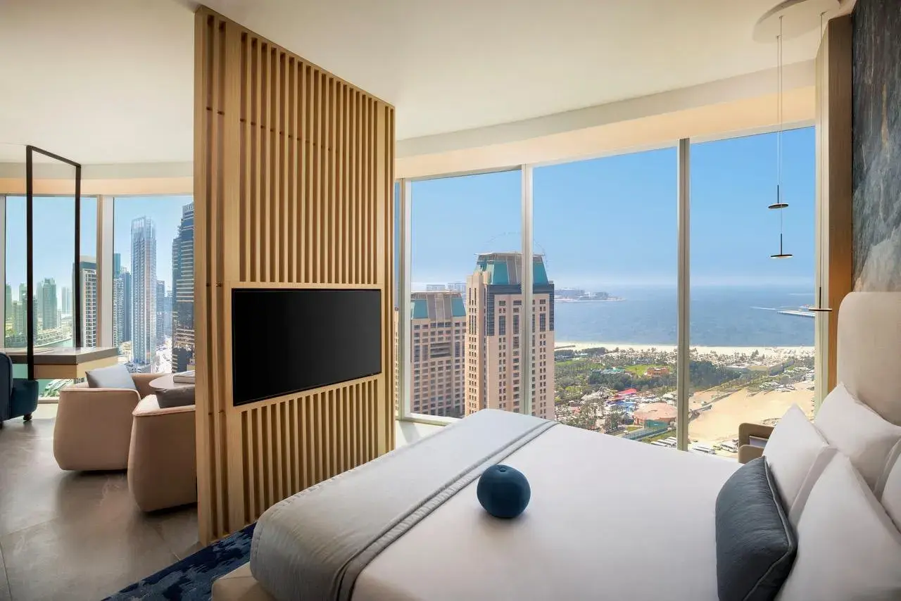 Modern hotel room with floor-to-ceiling windows offering views of the sea and Dubai skyline