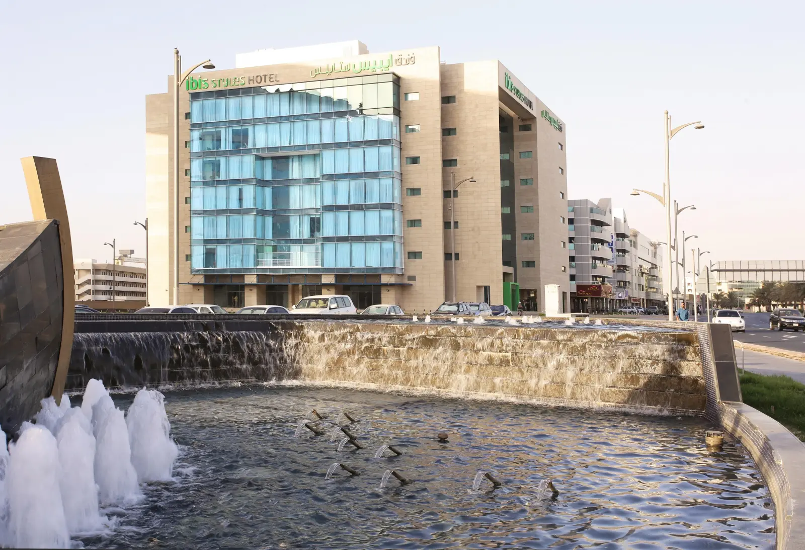 Exterior of Ibis Styles Dubai Jumeirah hotel with a fountain in the foreground.