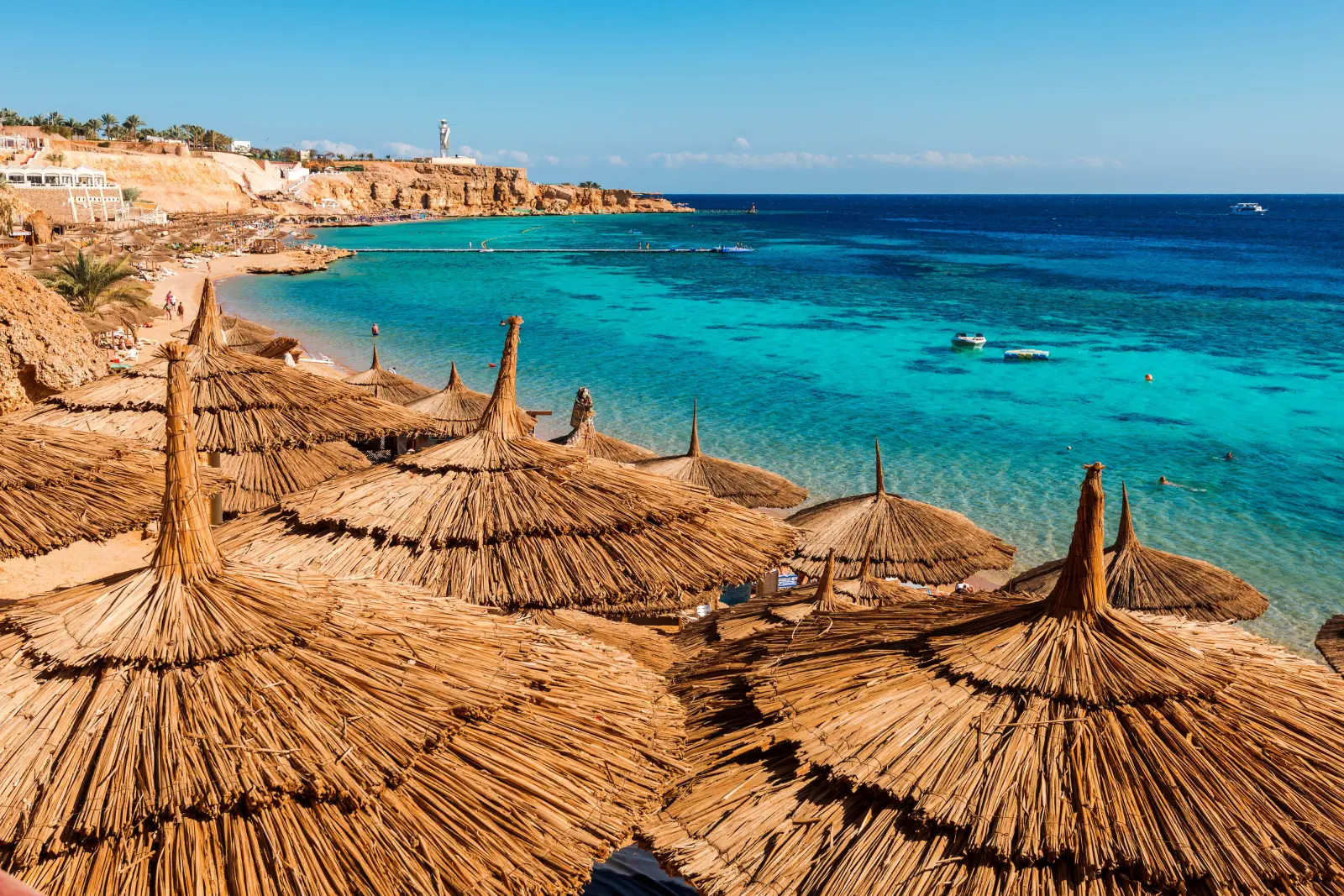 Straw beach umbrellas on the coast next to clear turquoise water.