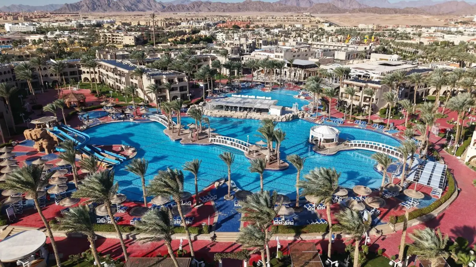 Aerial view of a large swimming pool with bridges and palm trees at a resort.